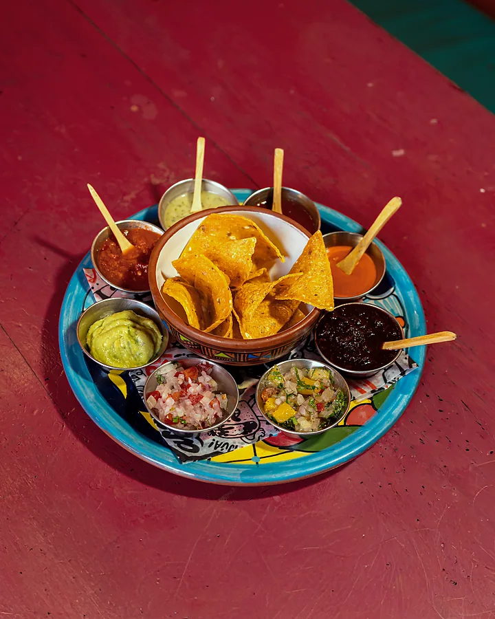 Totopos con guacamole, pico de gallo, frijol y salsas sobre la mesa roja del local