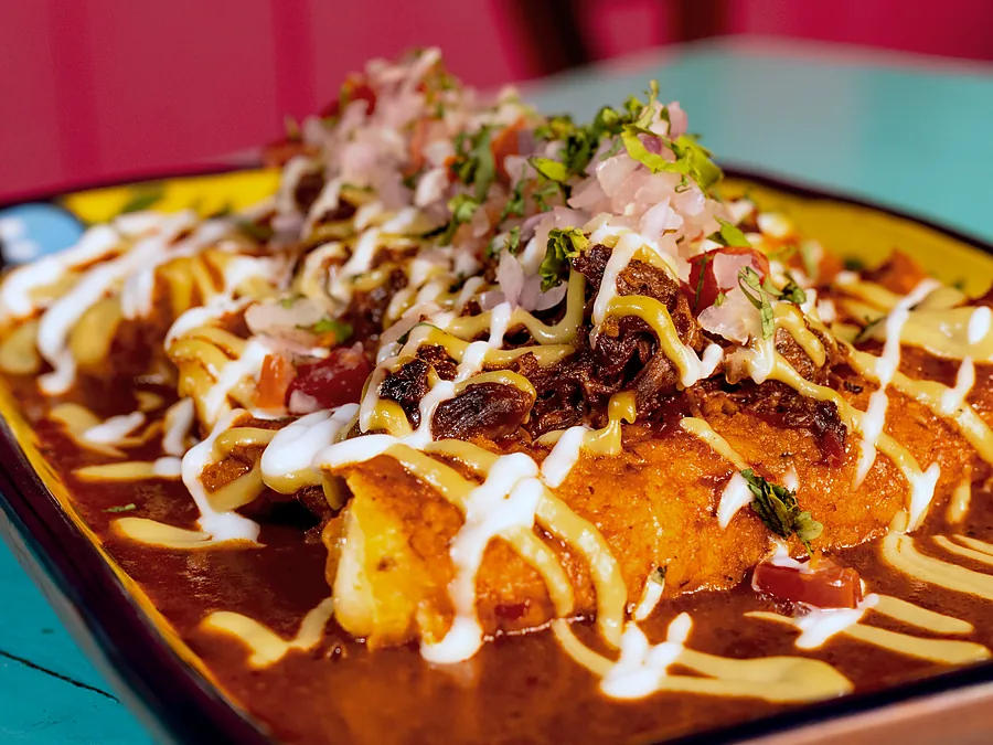 Flautas de birria de res bañadas en consomé con crema y cebolla encurtida