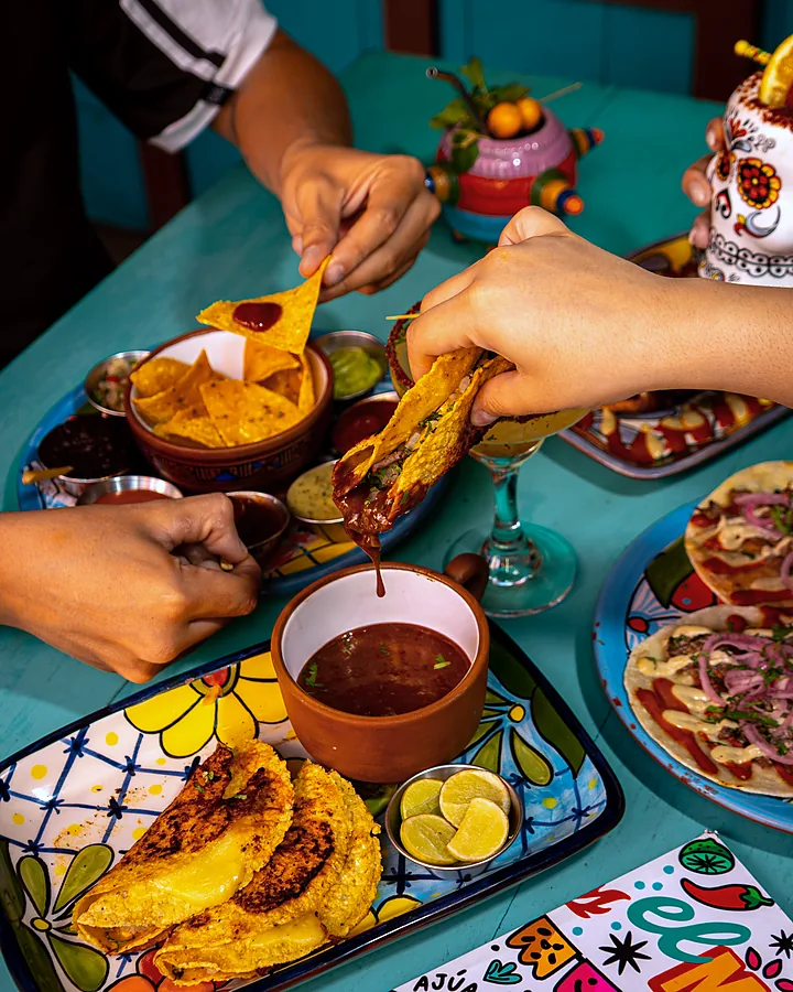 Manos compartiendo tacos y consomé en una mesa del local