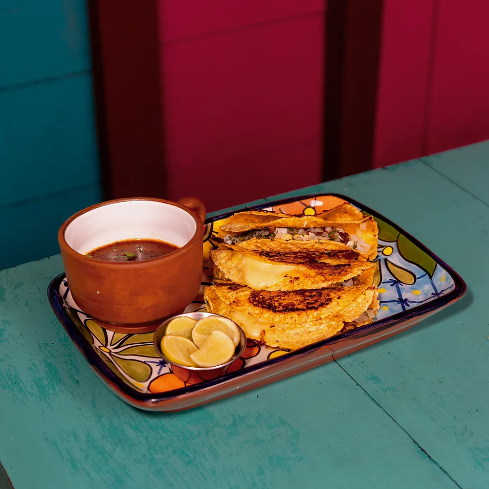 Tacos de birria de res con consomé y limón en un plato de talavera