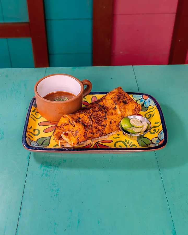 Plato de birria con su consomé en la mesa turquesa del local