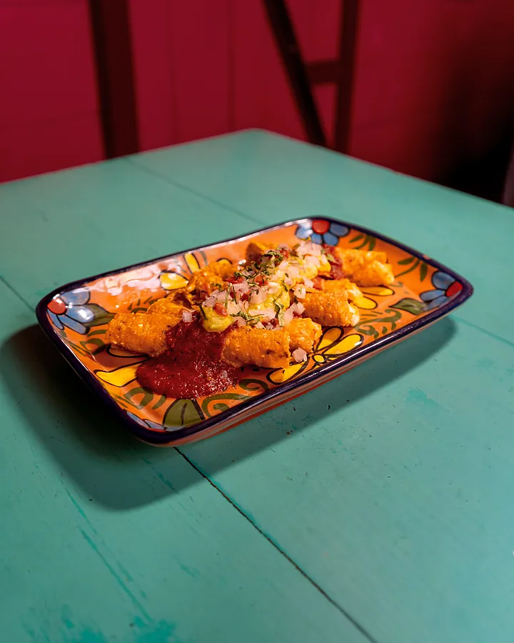 Flautas bañadas en salsa roja en una mesa turquesa del local