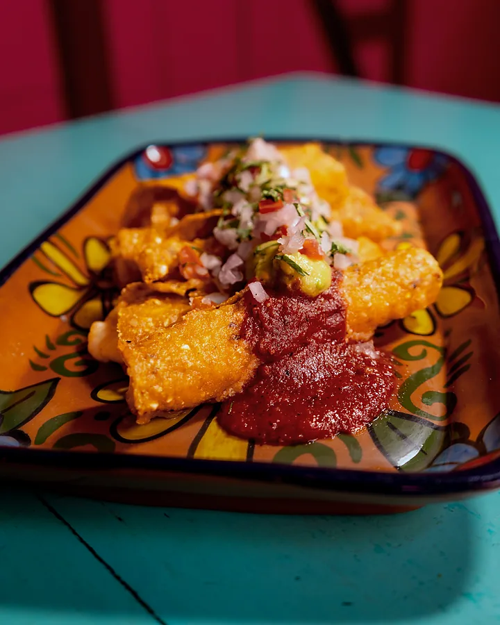Flautas con salsa roja, crema y cebolla encurtida en plato de talavera