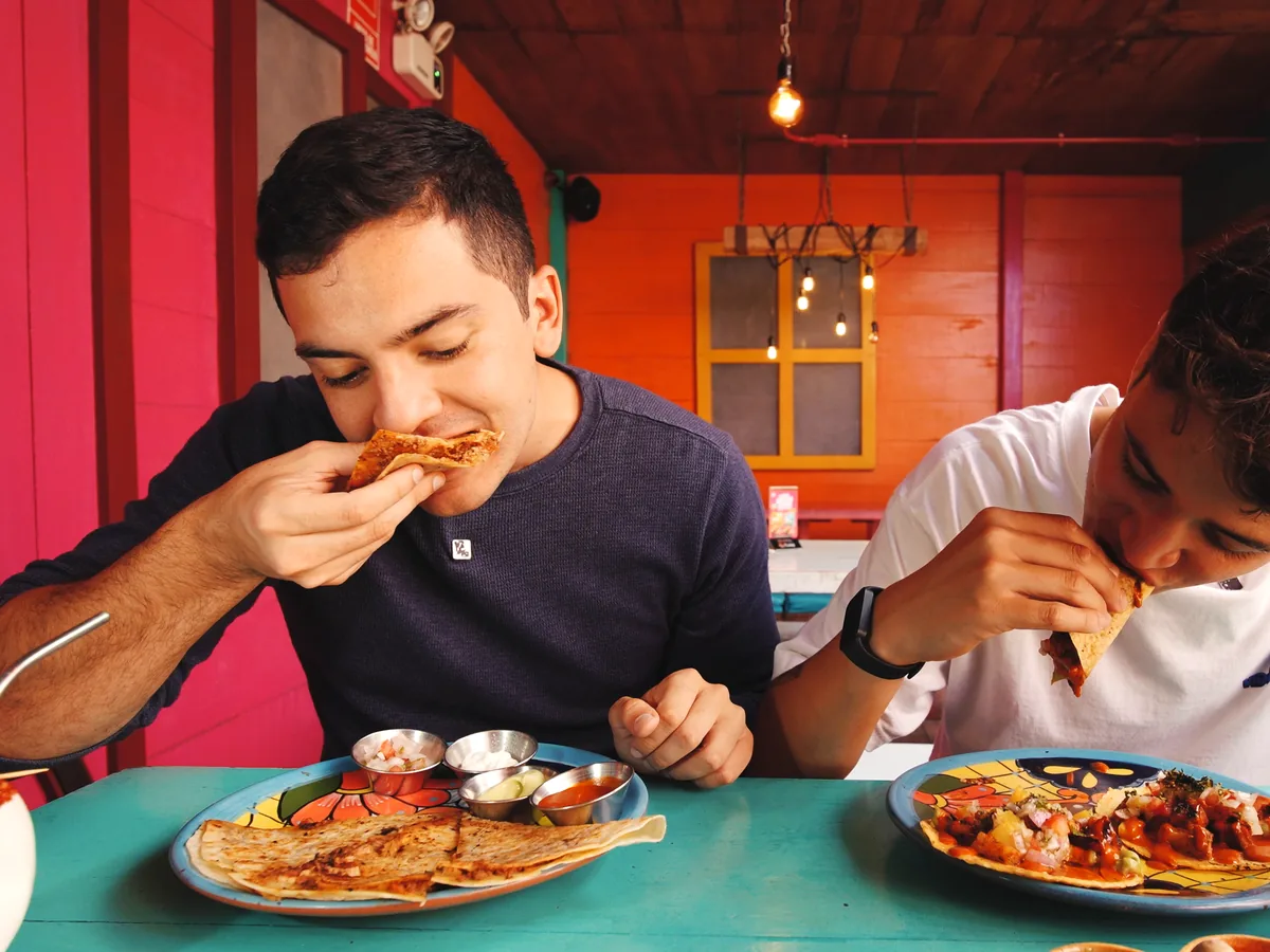 Dos amigos comiendo tacos con micheladas en el salón de colores del local